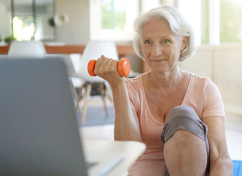 Senior woman doing fitness exercises at home through virtual class